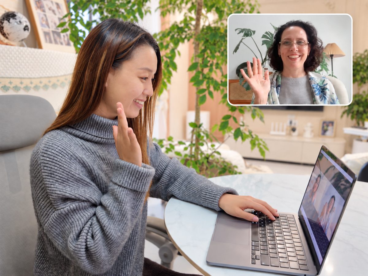 A teacher waving during a live online Chinese lesson with a student at her laptop